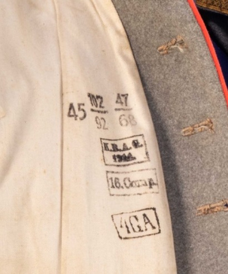 Macro photograph of an interior fabric label showing four ink stamps in a column: size stamps reading 45, 102 over 92, and 47 over 68 at the top; a boxed gothic-script stamp reading K.B.A.G. over the date 1914; a boxed stamp reading 16. Comp.; and a boxed stamp reading 4.G.A. at the bottom.